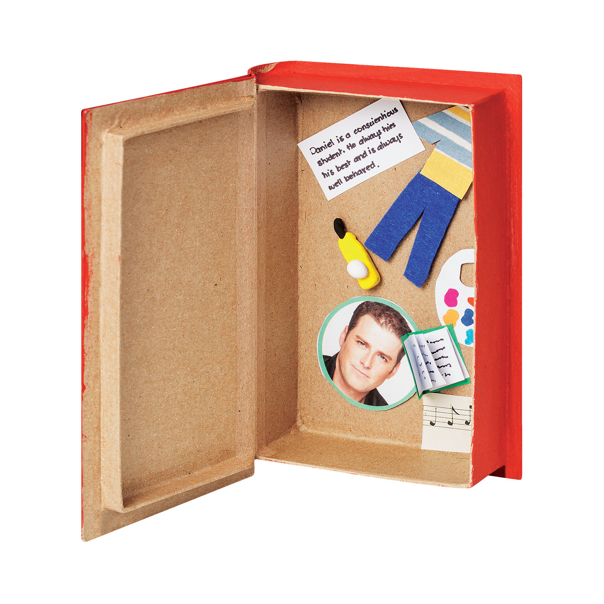 An open, painted red Zart Papier-mache Book box with a natural kraft brown interior, displaying a handwritten note, a photo of a man, small felt trousers, a paintbrush, a coloured palette, a music sheet, and a miniature open book glued inside as decorative embellishments.