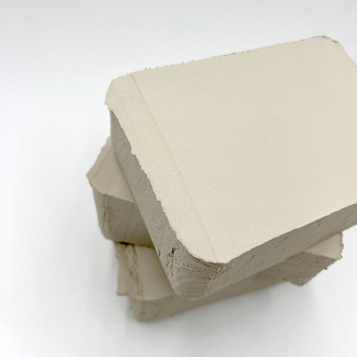 Stack of three pale cream clay blocks with smooth, flat surfaces and rough cut edges, showing the natural texture of Clayworks School White Clay. The blocks are arranged in an overlapping formation against a white background, displaying the clay's workable consistency.