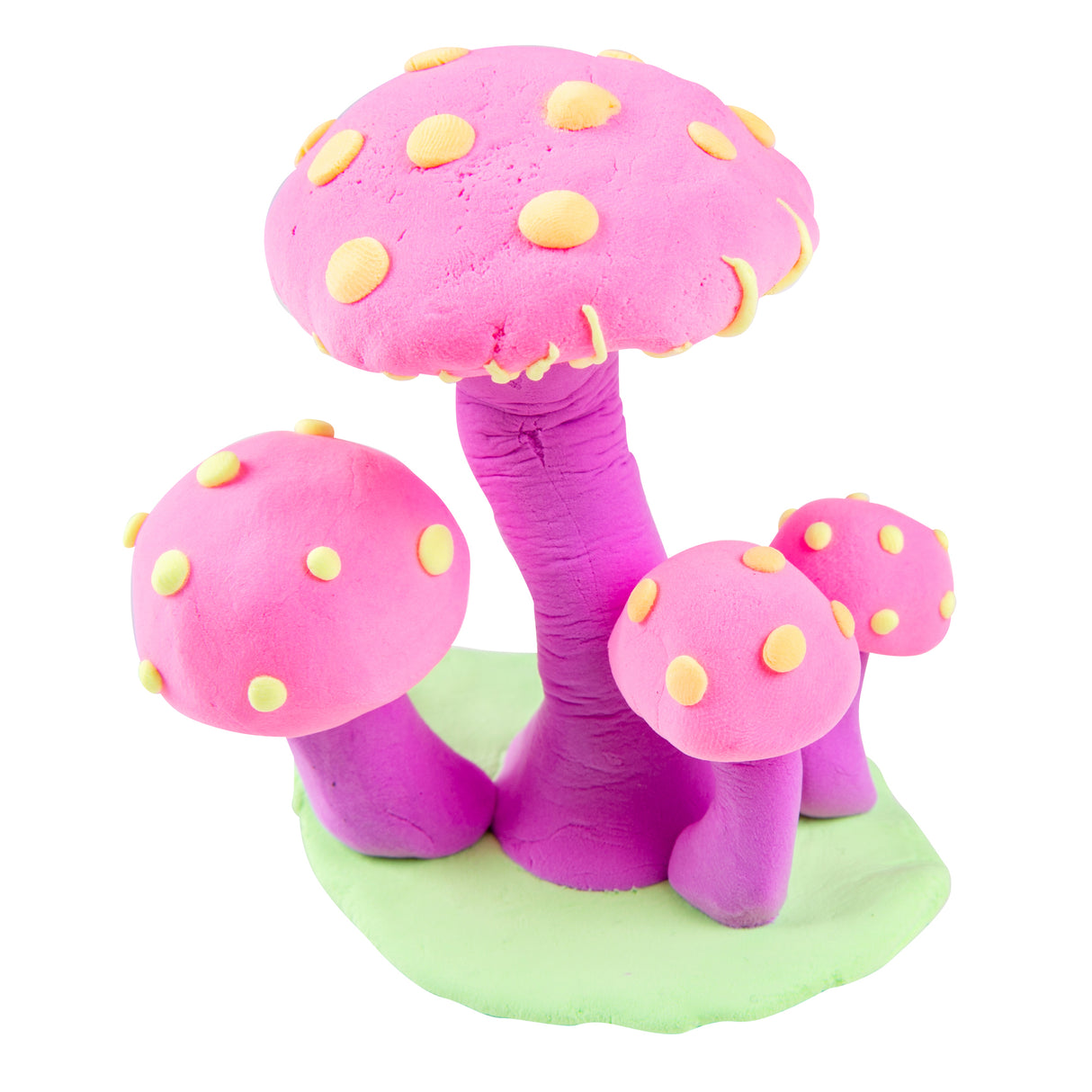 Three whimsical sculptural toadstools crafted from Paper Magiclay in vibrant neon pink and purple hues, featuring rounded caps decorated with yellow spots, textured cylindrical stems, and positioned on a soft green base against a white background.