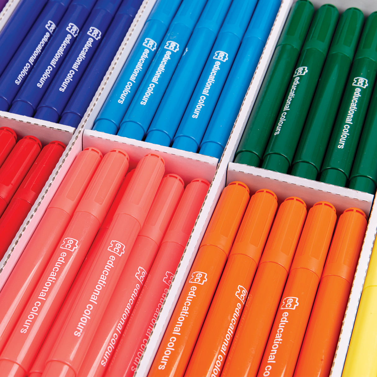 Close-up of assorted jumbo markers arranged neatly in white cardboard trays by colour, including blues, greens, reds, oranges and purples. Barrels are printed with “ec educational colours” in white text, highlighting the bold colours and thick, easy-grip design.