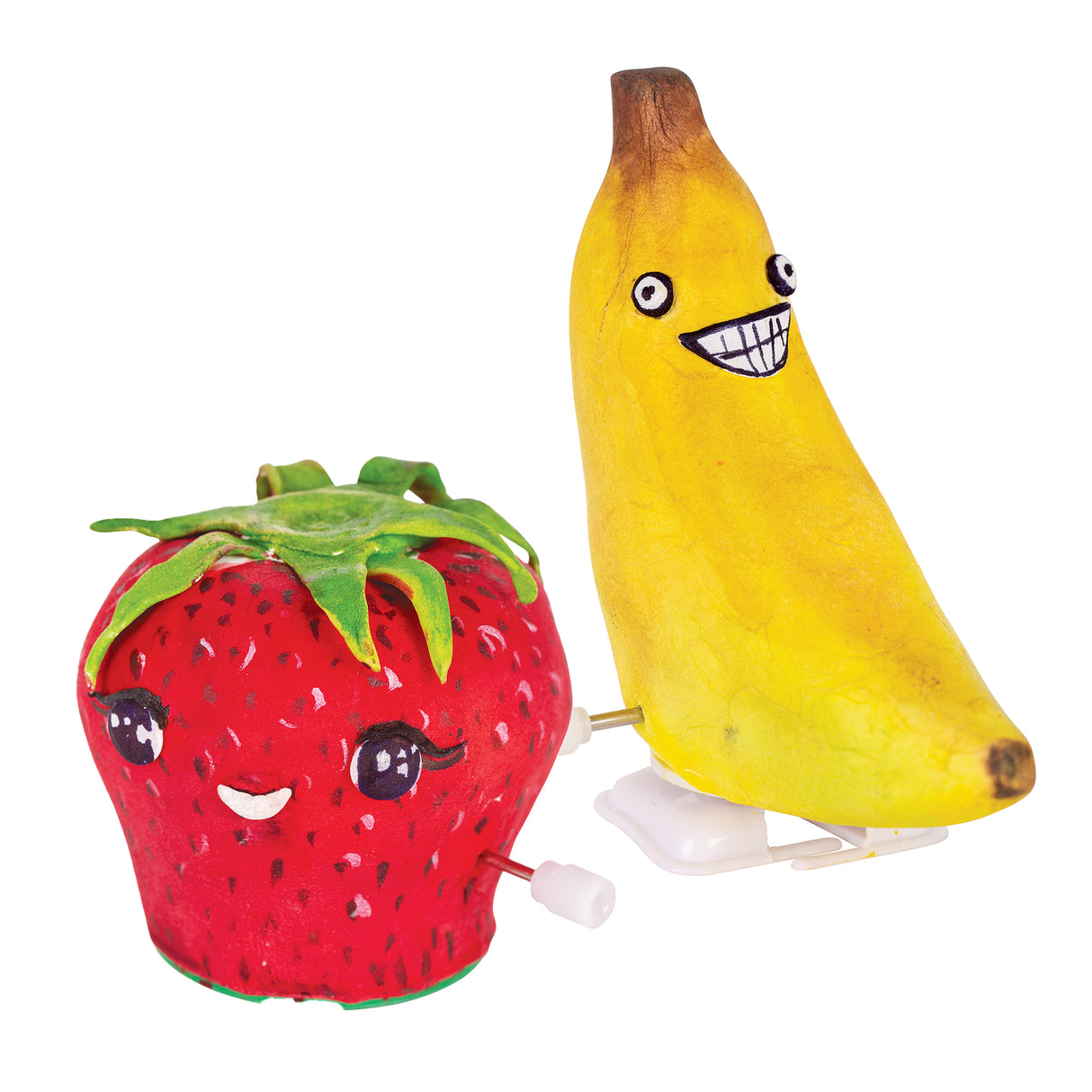 Decorated wind-up figures shaped like a strawberry and a banana feature bright painted surfaces with expressive cartoon faces. The strawberry is red with dotted seeds and green top, while the banana is yellow with shaded brown tips and a wide grin.