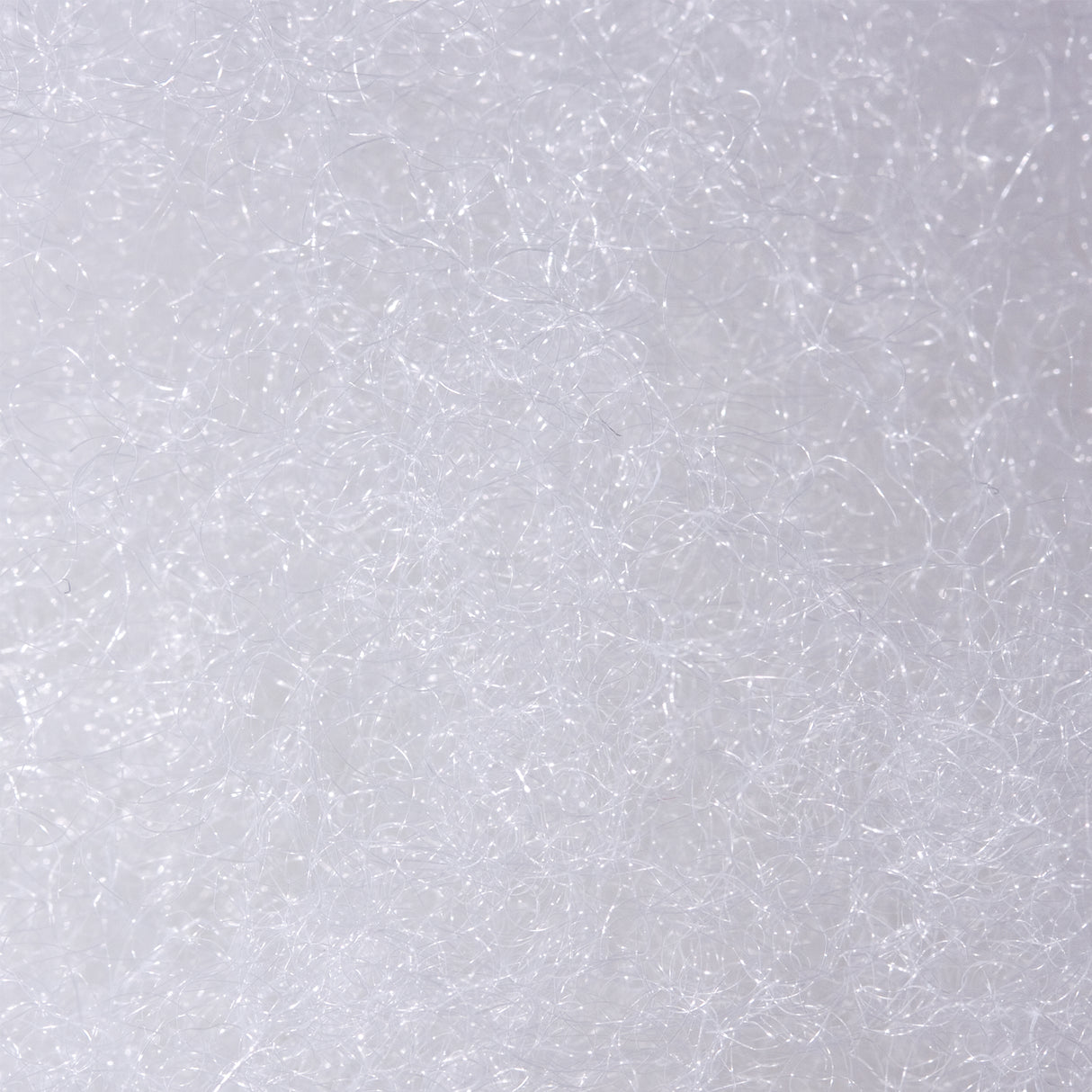 A close-up macro shot of white polyester filling, showing the loose, interwoven fibres in fine detail against a white background. Highlights the soft, lightweight texture of the filling material.