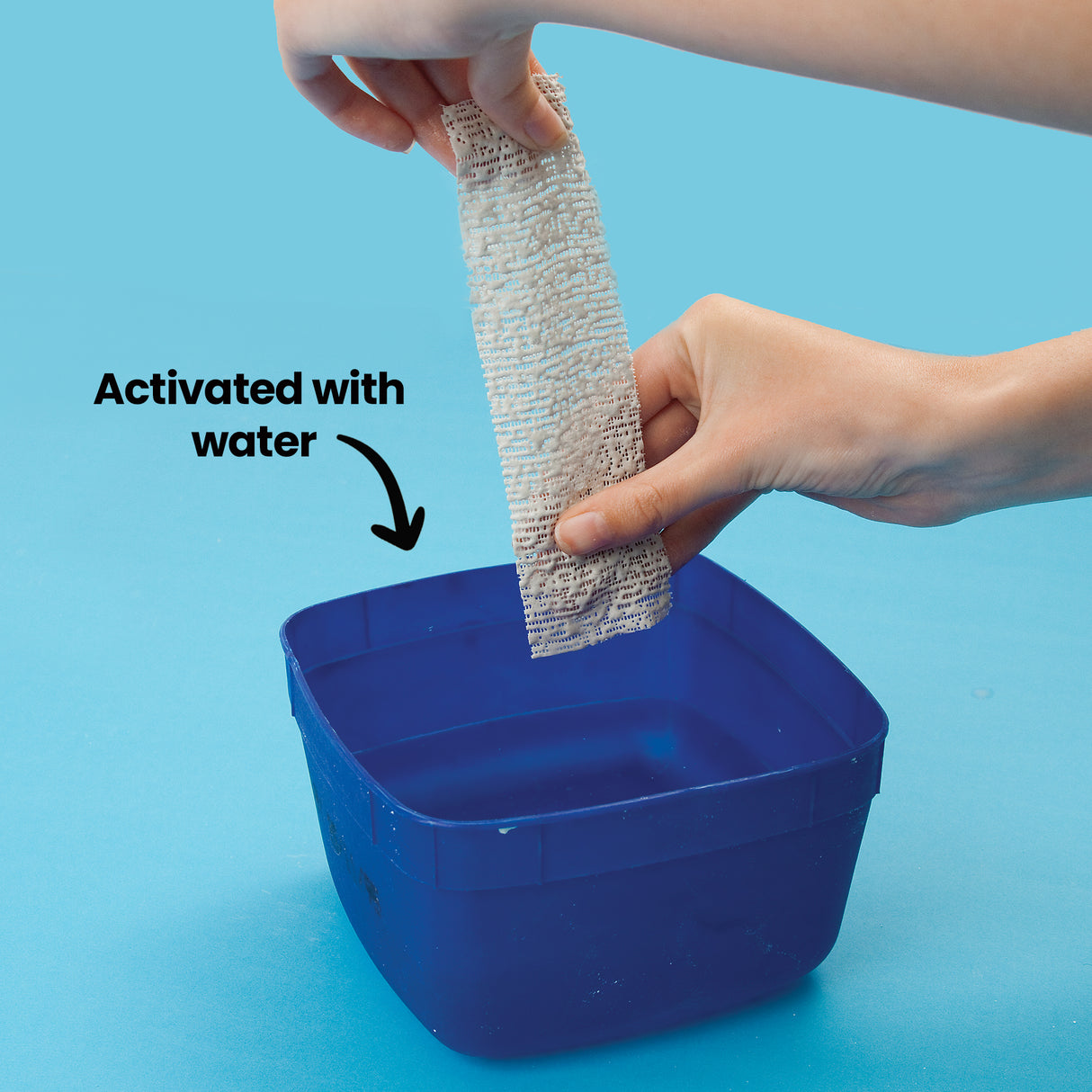Hands dip a strip of plaster bandage into a blue tub of water. Annotation text reads “Activated with water,” showing how the material is prepared before modelling.