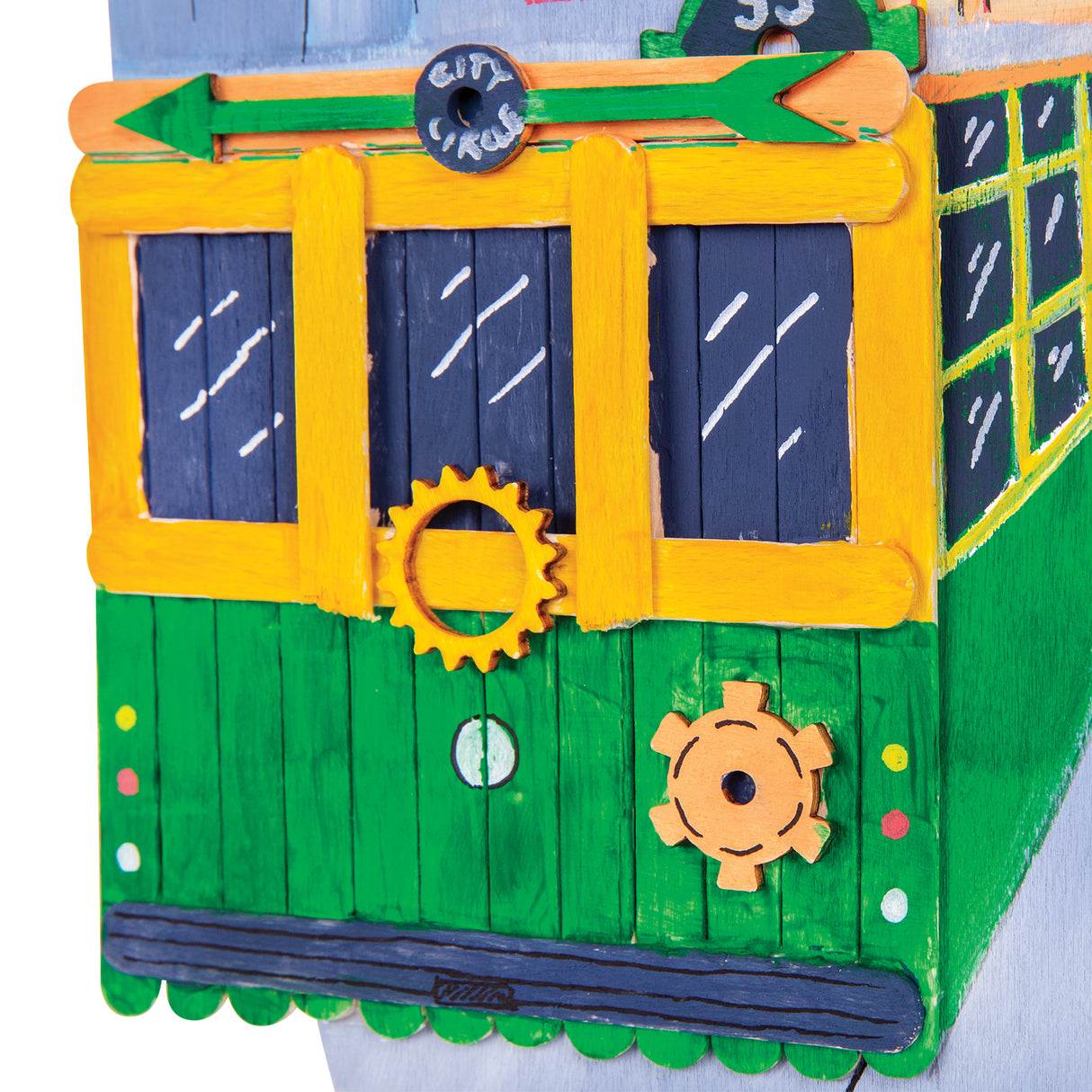 Close-up detail of a painted tram artwork constructed from wooden craft sticks, showing layered sticks, painted windows, gears and decorative elements.