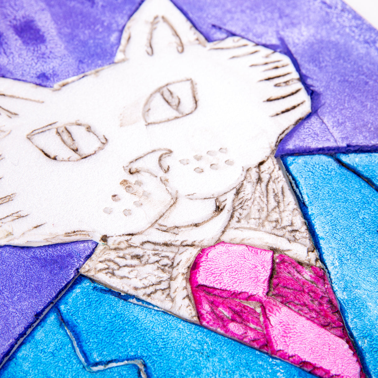 Close-up detail of a coloured print made from a foam plate, showing a cat’s face and upper body. The cat wears a blue suit jacket with a textured collar and a bright pink tie. Indented linework defines the eyes, whiskers and fur, set against a purple and blue background.