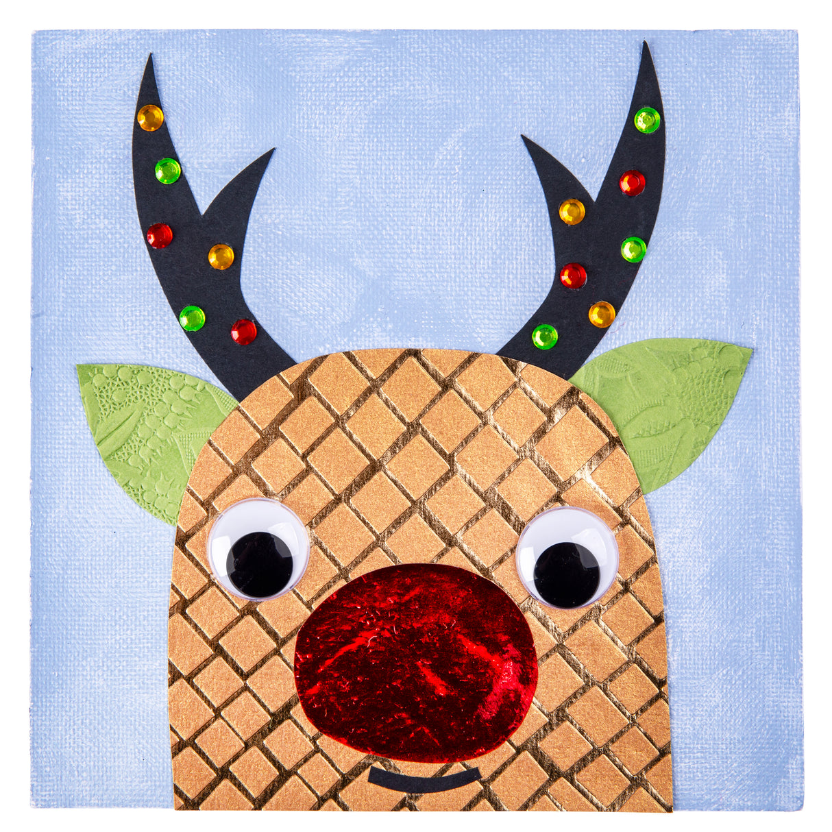 A sample artwork on a Zart Canvas Square Magnetic Board, depicting a reindeer face on a pale blue painted background. The design uses black antlers dotted with coloured gems, green textured paper ears, googly eyes, and a shiny red foil nose, demonstrating a mixed-media technique.