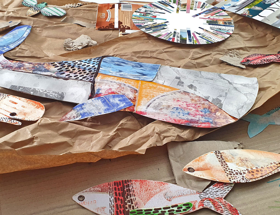 Zart Education Workshop-in-a-Box Upcycled Card and Paper collage scene featuring a large fish shape made from cut and layered magazine pages placed on crumpled brown paper. Surrounding it are smaller fish cut-outs decorated with colourful printed textures and dot patterns, along with a circular radial collage artwork in the background. The arrangement highlights recycled materials and creative upcycling techniques.