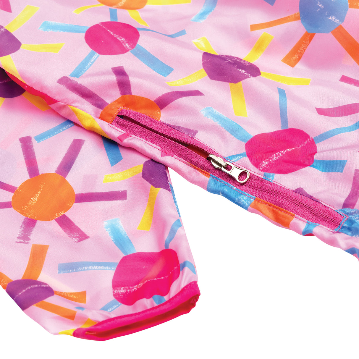 Vibrant pink art smock with bright sunburst pattern featuring circular centres in hot pink, purple, orange and blue with radiating brushstroke rays in yellow, light blue, purple and orange. Features a pink zipper closure detail and folded fabric showing the cheerful, painterly design.