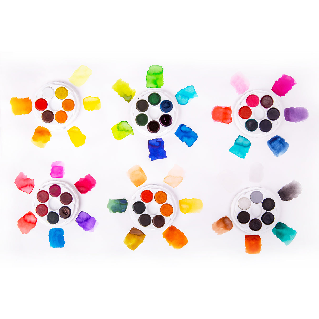 Six open Micador Brilliant Water Colours discs sit on white paper, each surrounded by matching painted swatches. The layout shows warm, cool and neutral colour groupings, with translucent washes, darker pooled edges, and irregular brush-textured rectangles.