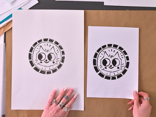 Two black-and-white lino prints a larger and smaller version feature a stylised cat face within a circular geometric border. Student works from the Zart Education On Demand lesson unit Animal Lino Print Inspired by Samantha Curcio, showcasing bold contrast and confident, expressive line work.
