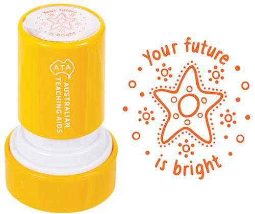 Bright yellow cylindrical self-inking stamp featuring the Australian Kids logo, displayed alongside an orange stamped impression showing a decorative star design surrounded by dots and circles with text reading "your future is bright"