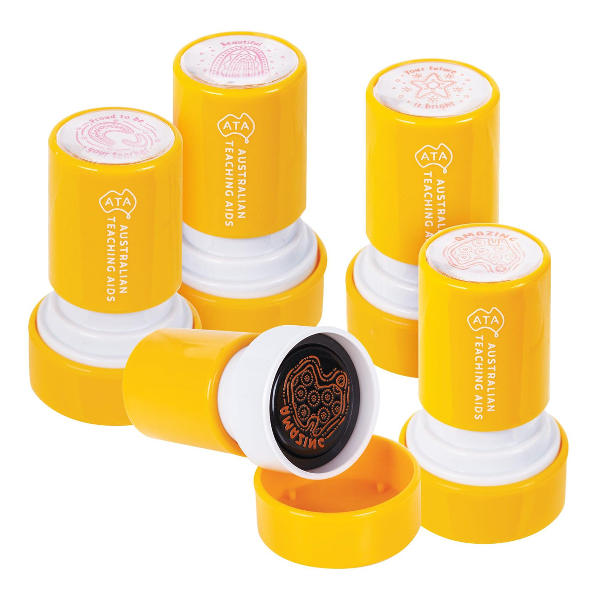 Five bright yellow cylindrical Australian Teaching Aids stamps arranged in a casual stack, each featuring white foam stamp bases with pink Indigenous-inspired designs including rainbows, stars, and native animals. One stamp displays an orange ink pad and black foam stamp surface with a detailed animal motif.