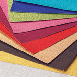 Zart Glitter Iron-On Sheets fanned out to reveal a vivid range of colours, including pink, teal, blue, green, magenta, red, gold, bronze, black, yellow and silver. Each sheet has a fine, densely packed glitter finish with a soft sheen, showcasing the full assorted colour palette.