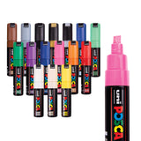 POSCA Chisel Tip Markers set of sixteen, shown standing with caps on in a staggered arrangement, covering a wide colour range including brown, grey, black, gold, blue, green, purple, navy, pink, orange, red, white, cream and yellow. A larger uncapped pink marker sits alongside, showing its chisel-shaped nib.
