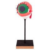 A sample artwork made using a Zart Wooden Base: a sculpted clay eyeball mounted on a thin black rod rising from the square base, its top surface painted black. The eyeball has a green iris with dark pupil, pink eyelid detail, dark lashes and a red tear duct.
