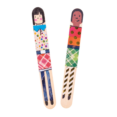 Two decorated Popstick Natural - Giant craft stick characters are displayed vertically against a pale grey background. The artworks feature hand-drawn faces, patterned washi tape clothing, metallic gold dots, colourful geometric designs, and painted striped legs with contrasting black shoes.