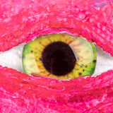 Close-up of a single realistic Creature Eye with yellow-green iris and black pupil set within vibrant pink textured sculpting material. The glossy dome eye features detailed colouring with orange and green tones, demonstrating how the eye can be embedded in creative projects to add dimension and character.