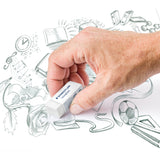 Hand holding a white Staedtler Rasoplast eraser while removing graphite pencil shading from detailed sketch illustrations on white paper. The drawing includes books, musical notes, flowers, sports equipment and abstract shapes, with visible soft pencil textures and clean erased areas surrounding the eraser.