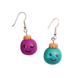 Two handmade earrings shown as sample artworks using Zart Jewellery Findings. Each earring features a round ball charm with a painted smiley face — one purple, one teal — topped with a small gold-toned cap. Both hang from silver shepherd hook findings attached by small jump rings.