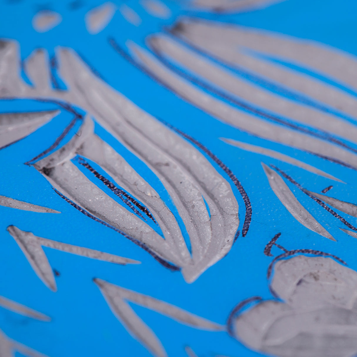 Close-up view of a carved blue Lino Tile Vinyl Double Sided surface showing leaf and petal shapes. The carved areas expose the lighter layer underneath, with fine cut lines and textured tool marks visible across the design.
