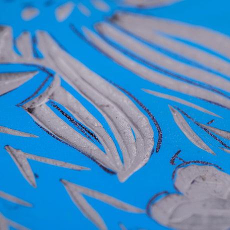 Close-up view of a carved blue Lino Tile Vinyl Double Sided surface showing leaf and petal shapes. The carved areas expose the lighter layer underneath, with fine cut lines and textured tool marks visible across the design.