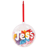 A Zart Plastic Bauble decorated as a sample keepsake, filled with scrunched rainbow tissue paper in pink, orange, yellow, blue and purple. White paper letters spelling "Jess" and small white snowflake dots are stuck to the clear surface, hung from a red ribbon loop.