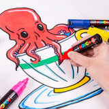 A hand holding a red POSCA Chisel Tip Marker, colouring in a green stripe on a drawn teacup beneath a cartoon red octopus. Blue, yellow and pink capped markers sit nearby on the partly finished illustration.