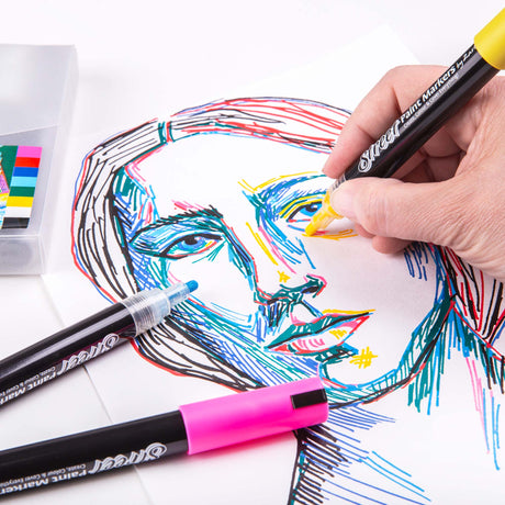 Hand using a yellow Zart Street Paint Marker to add bright strokes to a colourful line-drawn portrait. Other markers and the storage case sit nearby on the workspace.