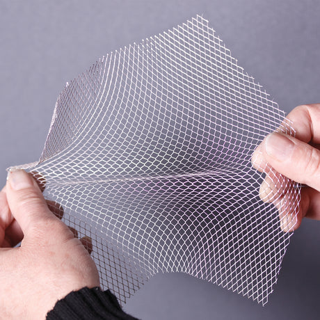 Flex-it Mesh (Medium) held between fingers, gently curved to show flexibility. The silvery aluminium strands form a tight diamond grid, catching light with a soft metallic sheen. Edges appear slightly jagged where cut, emphasising its thin, pliable texture.