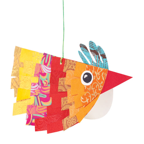 Colourful hanging bird collage made from layered Cartridge Paper Circles with textured and patterned paper strips in yellow, orange, red, pink and gold tones. The bird features a red triangular beak, blue patterned crest feathers, a large graphic eye and a green hanging string against a white background.