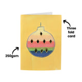 A decorated sample made using a Zart Cards and Envelopes Xmas Cut-Outs card, backed with a rainbow-striped bauble drawing dotted with small gold gem accents, set against a yellow card front. Text overlays read "Three fold card" and "250gsm".