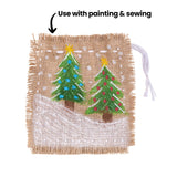 A square sample artwork on natural hessian fabric with frayed edges, decorated with a painted winter scene showing two green Christmas trees with yellow star toppers against a white snow ground and white dot details. An annotation reads "Use with painting & sewing" pointing to the fabric surface.