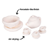 A miniature teapot, teacup and saucer set sculpted from Magiclay Porcelain Clay, annotated 'Porcelain-like finish' pointing to the smooth white surface, and 'Air-drying' pointing to the pieces. Delicate handles and lids are hand-shaped, showing the clay's fine detailing capability without kiln firing.