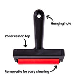 Front view of roller with annotation text reading Hanging hole, Roller rest on top and Removable for easy cleaning. Arrows point to the handle opening, flat resting edge, and red roller. Black frame and bright red rubber cylinder contrast against white background.