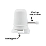 A close-up of a white wind-up walking mechanism highlights its structure with visible labels reading “Wind-up mechanism” and “Walking feet.” The textured dome casing sits above a simple base where the small plastic feet are positioned.