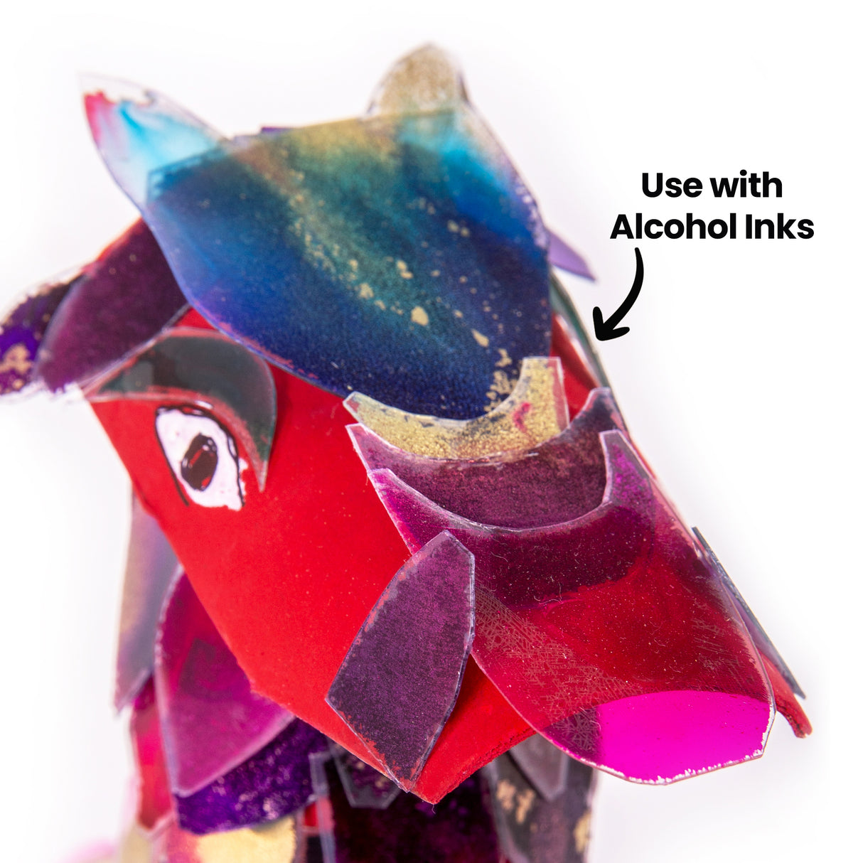 A close-up of the dragon creature made from Zart Acetate Heavyweight Sheets, showing overlapping scale pieces in blue, gold, purple, pink and red with a drawn eye. Annotated "Use with Alcohol Inks", highlighting the inked colour effects and speckled detailing on the translucent scales.