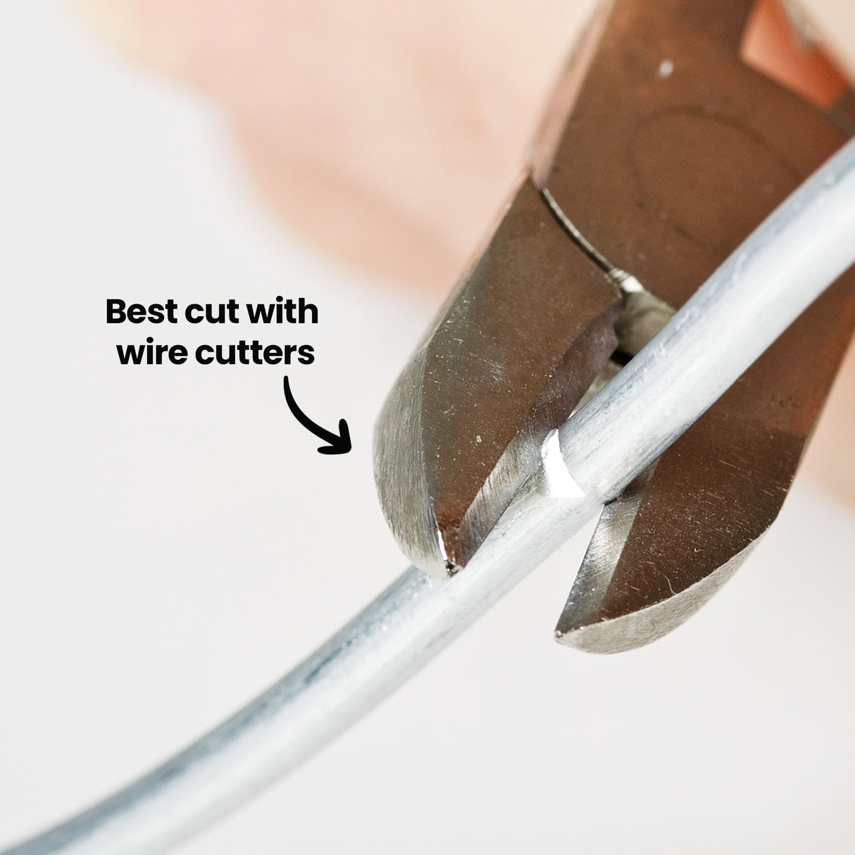 Close-up of Armature Wire being cut with wire cutters. On-image text reads Best cut with wire cutters with an arrow pointing to the cutting blades gripping the thick silver wire, demonstrating the recommended tool for clean trimming.