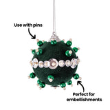 A green Zart Flocked Bauble decorated with metallic green pearl-topped pins and a band of silver gems with pearl centres. Text overlays read "Use with pins" and "Perfect for embellishments", highlighting the bauble's flocked surface as a base for pinned craft decorations.