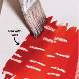 An annotated close-up of a red-orange watercolour wash painted over a wax-resist pattern of horizontal lines, using Eco Colour Liquid Food Dyes, with a paintbrush shown applying the colour. Labelled "Use with wax", demonstrating how wax resist creates a striped, textured effect.