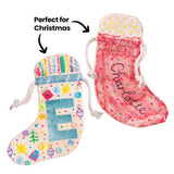 Two decorated Zart Calico Stockings: one with a glitter letter "E", stitched embroidery samples, painted snowflakes and stars, and buttons sewn on; the other dyed pink with a name embroidered in cursive and dotted bead-like accents. The annotation "Perfect for Christmas" points to both.