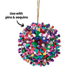A Zart Poly Deco Foam ball covered densely in colourful sequins and pin-topped beads in purple, pink, green, blue, gold and silver. It hangs from a gold thread against a white background, with an arrow annotation reading ‘Use with pins & sequins’.