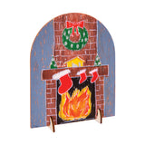 A hand-painted sample made using a Zart Desktop Message Board, depicting a brick fireplace with a wreath above the mantel, three red stockings, a small house and snow-dusted trees, and glowing flames below. The arched board stands on its two side legs.