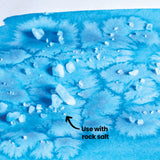An annotated close-up of a blue watercolour wash textured with rock salt crystals, using Eco Colour Liquid Food Dyes. The salt creates soft, crystalline blooming patterns across the paper. Labelled "Use with rock salt", demonstrating the technique's frosted, mottled visual effect.
