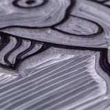 Extreme close-up of a Mastercut Print Lino Round surface showing carved channels and fine line texture. Raised outlines appear dark while the carved areas show lighter grey highlights. The detailed cut marks demonstrate how the lino holds crisp grooves for printmaking.