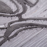 Macro close-up of carved lino surface showing recessed grooves and raised shapes forming curved lines. Fine tool marks and small flecks are visible within the cut areas. Subtle tonal variation appears between inked recesses and lighter raised sections.