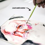 A hand using a wet brush to activate and blend Artline Liquid Crayons on a portrait drawing, creating soft watercolour washes in red and pink tones. An annotation reads "Just add water," demonstrating the product's water-reactive properties.