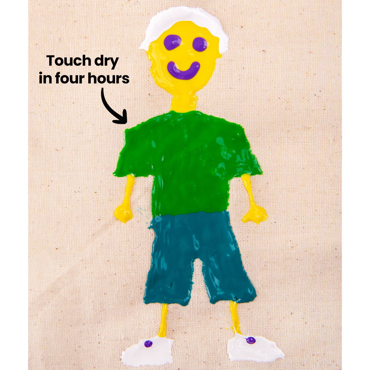 A raised puffy paint figure of a smiling person on natural calico fabric, with a yellow head and hands, white hair and shoes, purple facial features, a green top and teal shorts. Black text and an arrow read “Touch dry in four hours”, pointing toward the shoulder area.