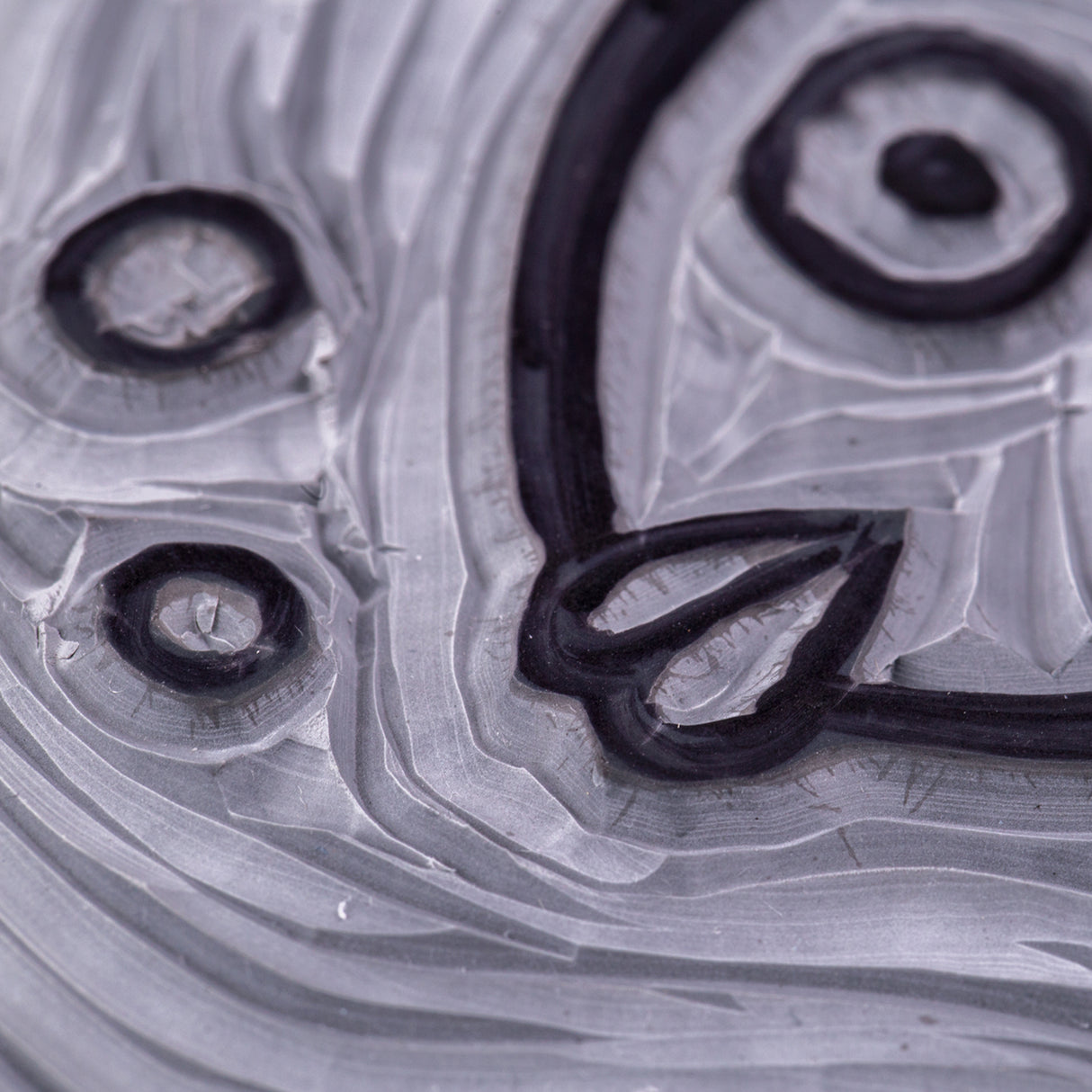 Extreme close-up of a carved Mastercut Print Lino Round block showing raised black outlines and recessed grey carved areas. The detailed grooves form part of a fish design with bubbles and curved lines. Fine cut marks and layered carving textures highlight the block’s ability to hold crisp linework.