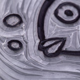 Extreme close-up of a carved Mastercut Print Lino Round block showing raised black outlines and recessed grey carved areas. The detailed grooves form part of a fish design with bubbles and curved lines. Fine cut marks and layered carving textures highlight the block’s ability to hold crisp linework.
