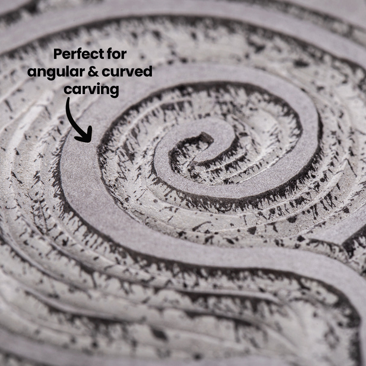 Close-up of a carved spiral design in a Silk Cut Lino Tile. Annotated text reads “Perfect for angular & curved carving,” pointing to the clean channels and textured tool marks created during the carving process.